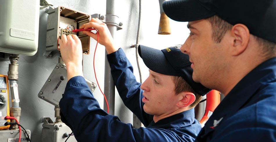 Male worker supervises young male apprentice doing electrical work (apprentices)