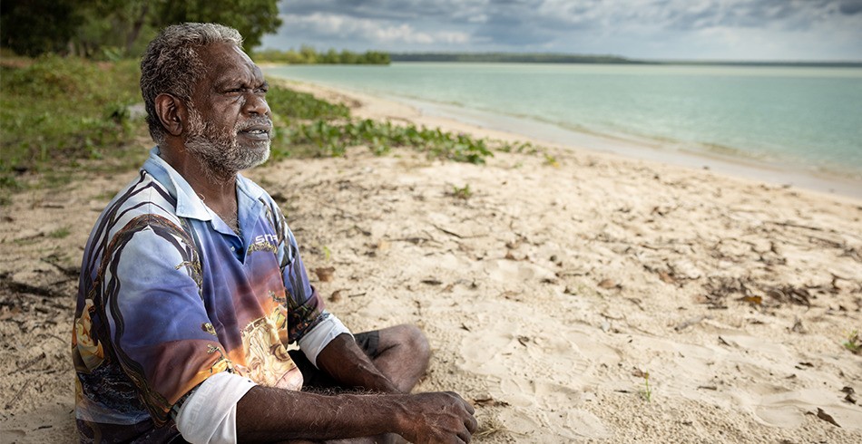 Tiwi Islander and plaintiff Dennis Tipakallipa sitting on the beach looking out at the sea (santos barossa)