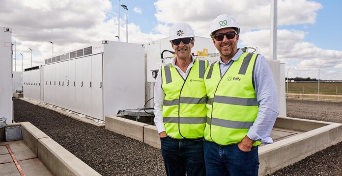 Two executives in high-vis vests and hard hats stand in front of battery system smiling (federation edify)