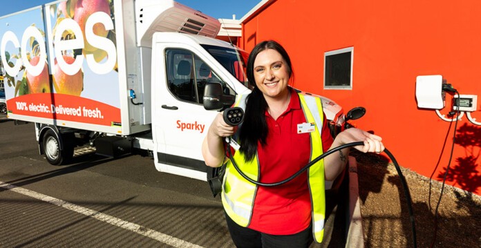 Smiling female worker from the Coles Online team holds EV charger with new electric van in background