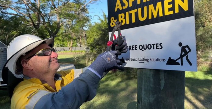 Energex worker in hard hat and safetywear uses pliers to remove unsafe sign from power pole