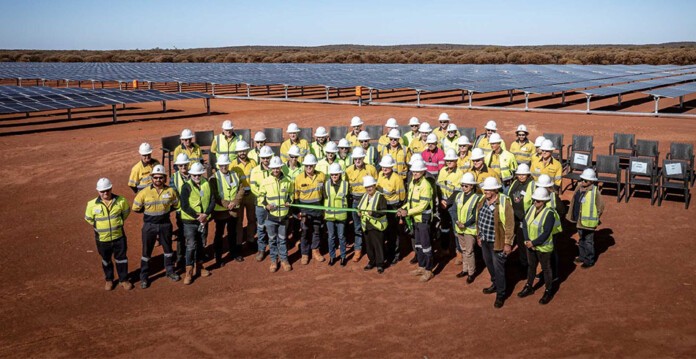 Pacific Energy and Westgold staff in high-vis vests and hard hats pose for photo in front of Tuckabianna solar farm