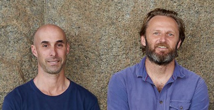 Two smiling men leaning against granite wall (motion)