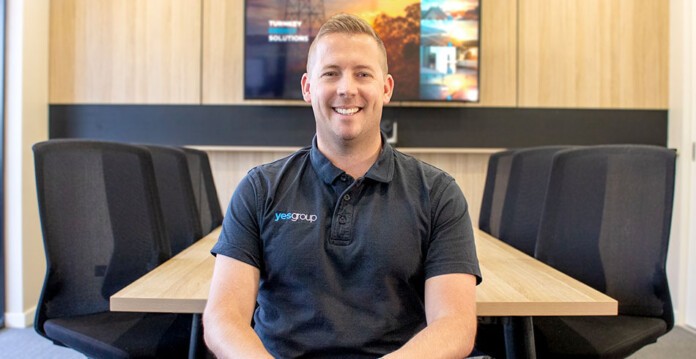 Man wearing YES Group polo shirt sits smiling in board room