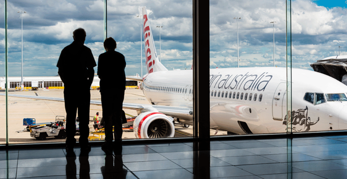 A man and woman stand at windows overlooking the tarmac at Melbourne Airport (AGL flexible demand)