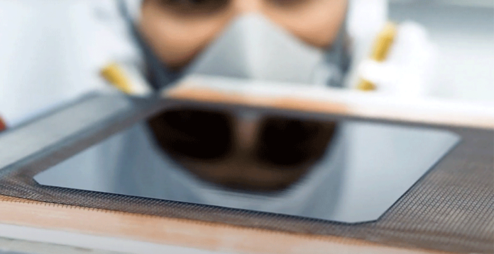 Man in protective lab gear stands behind Sundrive solar cell