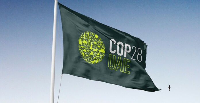 Flag waving against blue sky with COP28 logo (fossil)