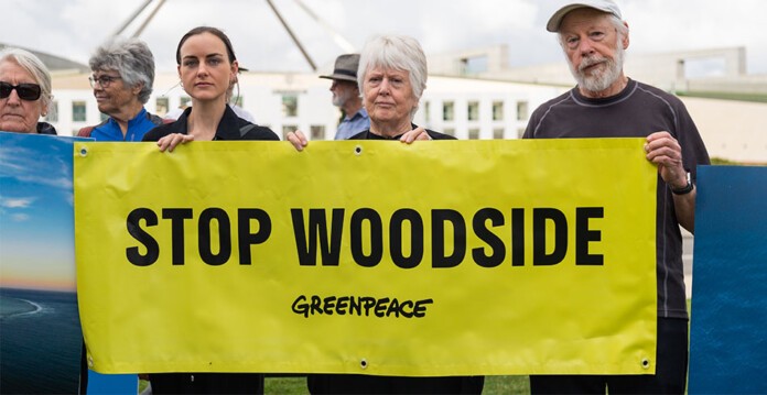 Greenpeace activists hold yellow sign saying STOP WOODSIDE outside Parliament House in Canberra