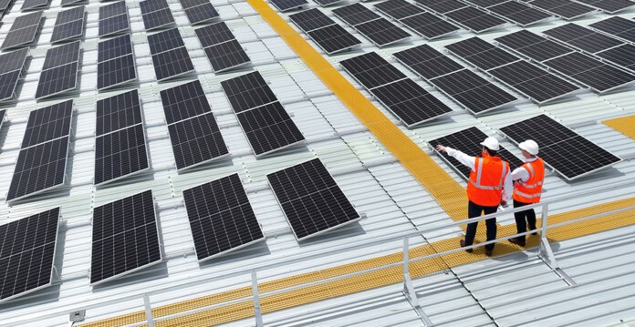 Two men in hard hats and high-vis wear stand on roof pointing at solar panels (stockland energy bay partnership)