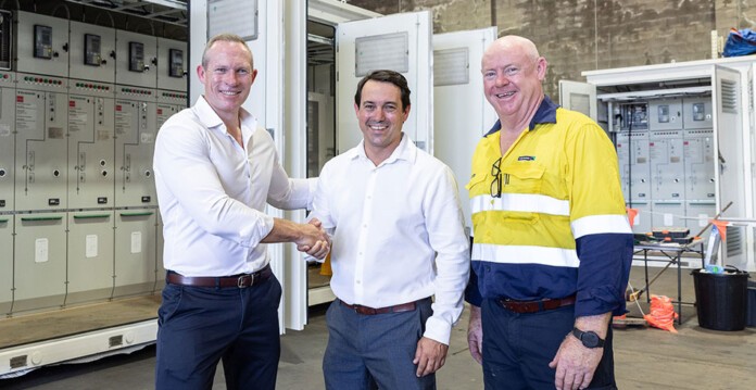 Three smiling men shake hands in front of substation equipment at TGOOD's new facility in Brisbane