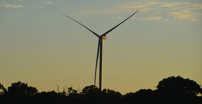 Large wind turbine silhouette against dusk sky with trees below (GE Squadron)