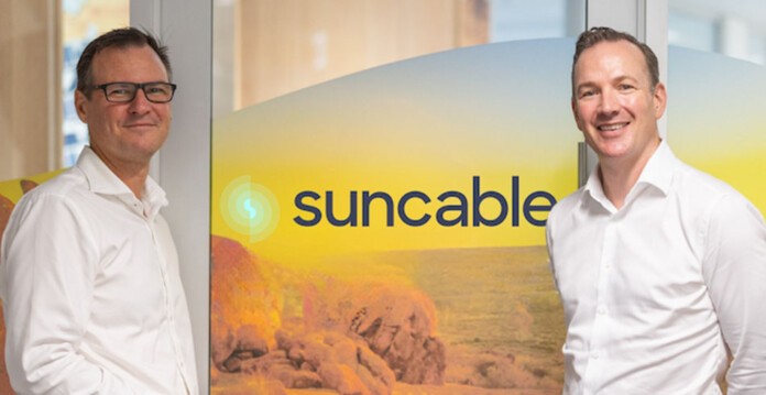 Two smiling male executives stand in front of SunCable signage