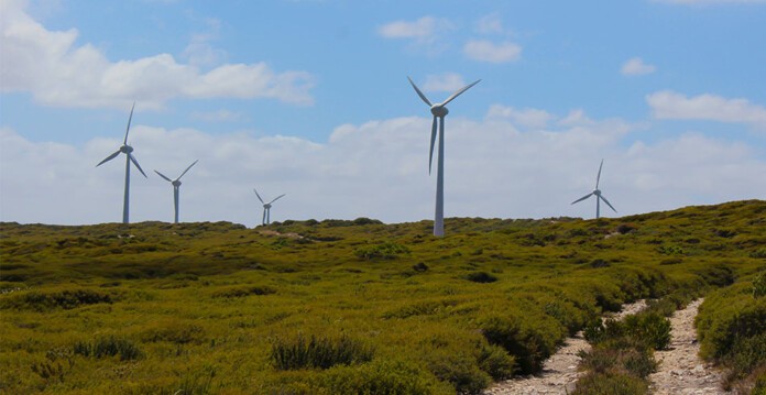 Wind turbines on grassy hill with blue sky overhead