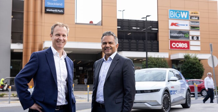 Two executives in suits outside a Stockland shopping centre with AmpCharge EV fast charger in background